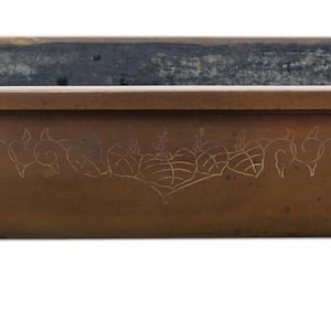 May include: A rectangular bronze planter with ornate detailing. The planter features a decorative floral design etched on the front and rests on four curved feet. The interior has a darker patina.