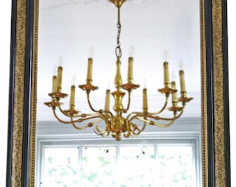May include: A rectangular mirror with a black frame and gold filigree detailing. The mirror reflects a gold chandelier with multiple candle-shaped lights. The frame has rounded corners and a black inner border.