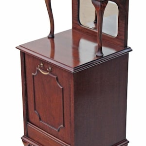 Op de afbeelding: Een donkerbruin houten nachtkastje met een kleine spiegel en een plank. De kast heeft een lade met een messing handvat en gebogen poten. Het hout heeft een glanzende afwerking.