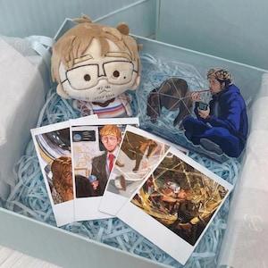 May include: A gift box containing a tan plush doll with glasses, an acrylic standee of a person in a blue jacket eating, and four rectangular photo prints featuring illustrated scenes of people in various settings, all nestled on light blue paper shreds.