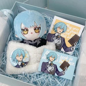 May include: A gift set containing a plush doll with light blue hair and golden eyes, a circular pin, and two rectangular cards. The cards feature an illustration of a character with light blue hair holding a book with the text May you find your book in this place.