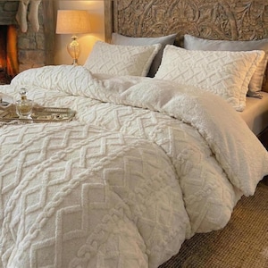 Peut inclure: Ensemble de literie crème avec un motif géométrique texturé. L'ensemble comprend une couette, des oreillers et un plateau décoratif avec un flacon de parfum. Le lit a une tête de lit en bois sculpté.