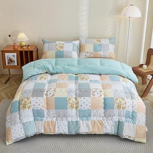 Puede incluir: Un edredón patchwork y dos fundas de almohada a juego en tonos azules, amarillos y melocotón. El edredón presenta una variedad de patrones cuadrados, incluyendo estampados florales y colores lisos. La capa superior es azul claro.