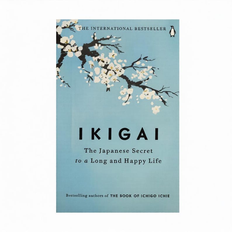 May include: A book cover with a light blue background features the title "IKIGAI" in large black letters. The cover includes a branch with white flowers and the text "The Japanese Secret to a Long and Happy Life."