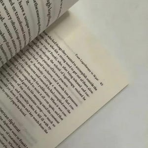 May include: Open book with text from "From Logotherapy to Ikigai" on a cream-colored page. The text is in black, with the page slightly angled. The book's pages are visible, with the text on the left page blurred.