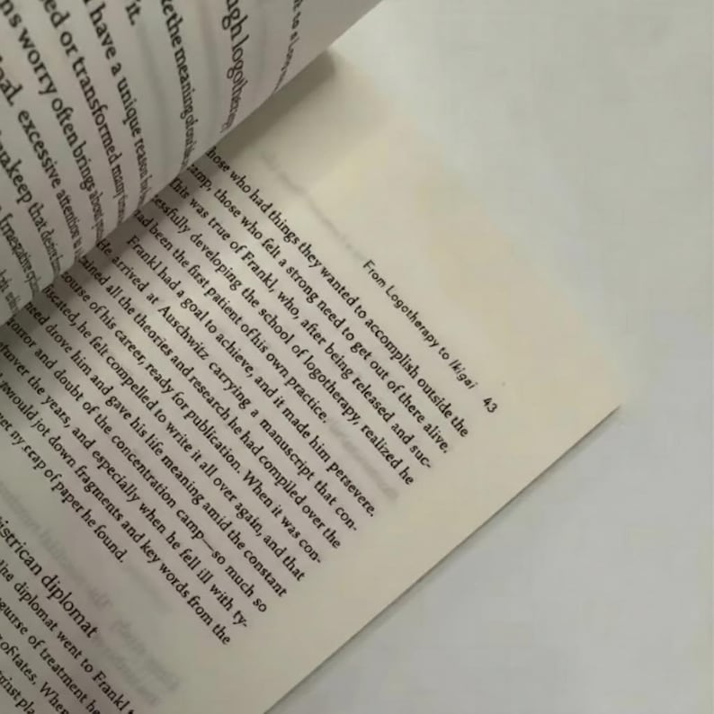 May include: Open book with text from "From Logotherapy to Ikigai" on a cream-colored page. The text is in black, with the page slightly angled. The book's pages are visible, with the text on the left page blurred.
