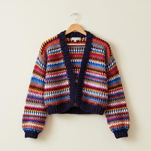 May include: A vibrant, open-front crochet cardigan with a striped design in red, blue, yellow, and white. The cardigan features long sleeves and a navy blue trim. It is suspended from a wooden hanger.