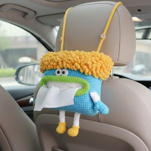Può includere: Un'originale e fatta a mano custodia per scatola di fazzoletti da auto, con corpo blu, capelli gialli e rifiniture verdi. La custodia ha gambe bianche con scarpe gialle ed è sospesa dal poggiatesta dell'auto tramite cinghie gialle.