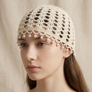 Peut inclure: Coiffe en crochet de couleur crème avec un motif ajouré délicat. La coiffe est ornée de petites perles de faux-semblant pendantes le long du bord inférieur. Cet accessoire ajoute une touche d'élégance vintage.