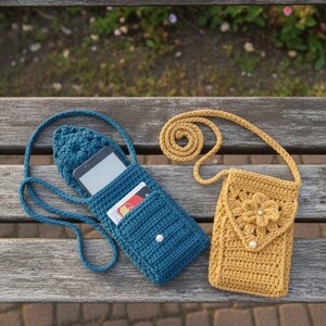K&ouml;nnte beinhalten: Zwei handgefertigte geh&auml;kelte Umh&auml;ngetaschen. Eine ist blau und enth&auml;lt ein Tablet und eine Karte. Die andere ist senfgelb, mit einem Blumendesign und einem Perlenakzent. Beide haben lange Riemen und werden auf einer Holzbank ausgestellt.
