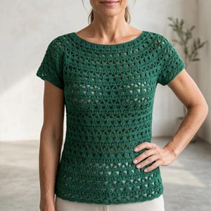 May include: A short-sleeved, dark green crochet top featuring a repeating triangular pattern throughout the garment. The top has a wide, rounded neckline and a semi-sheer construction with a consistent, intricate stitch design across the front.