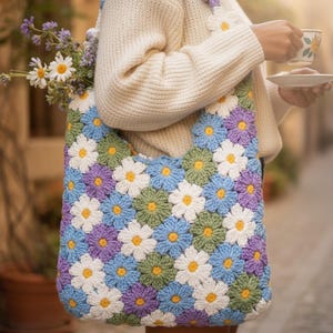 May include: A crocheted tote bag featuring a daisy pattern in white, blue, green, and purple. The bag has a shoulder strap and is filled with flowers. The bag is a vibrant accessory.