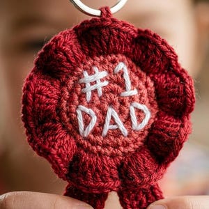 Può includere: Portachiavi fatto a mano all'uncinetto rosso a forma di rosetta. Il centro presenta il testo ricamato bianco «#1 DAD». Il portachiavi ha un anello in metallo argentato per attaccare le chiavi.