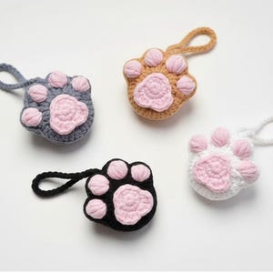 Peut inclure: Quatre objets en forme de patte, crochetés en gris, beige, noir et blanc. Chaque patte a des coussinets roses et une boucle pour suspendre. Ces articles faits à la main sont probablement décoratifs ou fonctionnels.