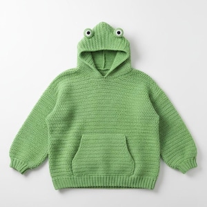 May include: A green, crocheted hoodie with a frog design. The hood features two large, round eyes. The sweater has long sleeves and a front pocket. The overall design is a solid, light green colour.