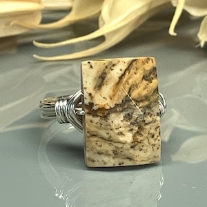 Peut inclure: Une bague en fil d'argent avec une pierre rectangulaire marbrée de brun et de blanc.