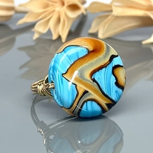 May include: A gold wire ring with a blue, brown, and white glass bead. The bead has a swirling pattern.