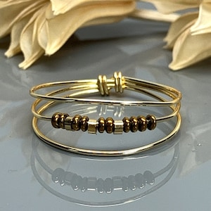 May include: A gold ring with three bands and a row of brown beads.
