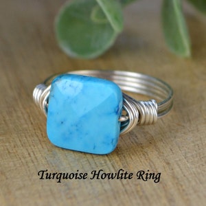 May include: A silver wire-wrapped ring featuring a square, faceted turquoise howlite stone. The ring's band is made of multiple strands of silver wire. The text "Turquoise Howlite Ring" is displayed below the ring.