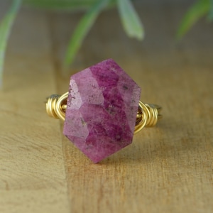 May include: A gold wire wrapped ring featuring a large, faceted, pink ruby gemstone.