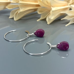 May include: A pair of silver hoop earrings with a dangling teardrop-shaped ruby gemstone on each earring.