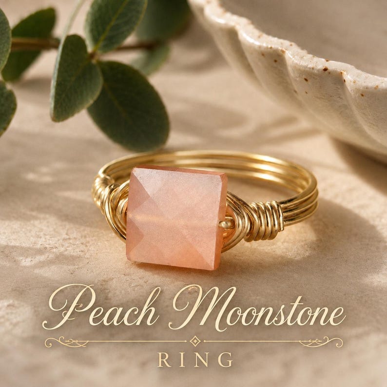 May include: A gold wire-wrapped ring featuring a square-cut peach moonstone gemstone. The band is constructed from multiple strands of thin gold wire coiled around the base of the stone. The text Peach Moonstone RING is printed below.