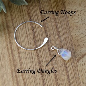 Pode incluir: Brincos de argola de prata com um pingente de pedra da lua. Os brincos de argola s&atilde;o abertos e curvos. O pingente de pedra da lua &eacute; enrolado em arame e tem uma apar&ecirc;ncia perolada. O texto na imagem diz "Earring Hoops" e "Earring Dangles".