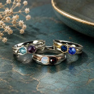 May include: Three wire-wrapped rings featuring faceted crystal beads. One ring has light blue and purple beads, another has dark blue beads, and the third has a white iridescent bead paired with a dark red bead, all set on metallic bands.