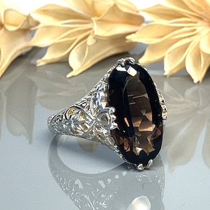 May include: A silver ring with an oval-shaped smoky quartz gemstone set in a filigree design.