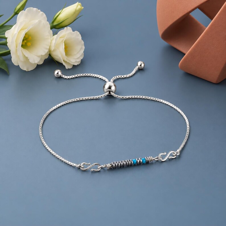 May include: A silver box chain bracelet featuring an adjustable sliding bead closure. The center bar is decorated with a series of small metallic silver rings interspersed with two bright turquoise blue beads, finished with S-shaped metal links.