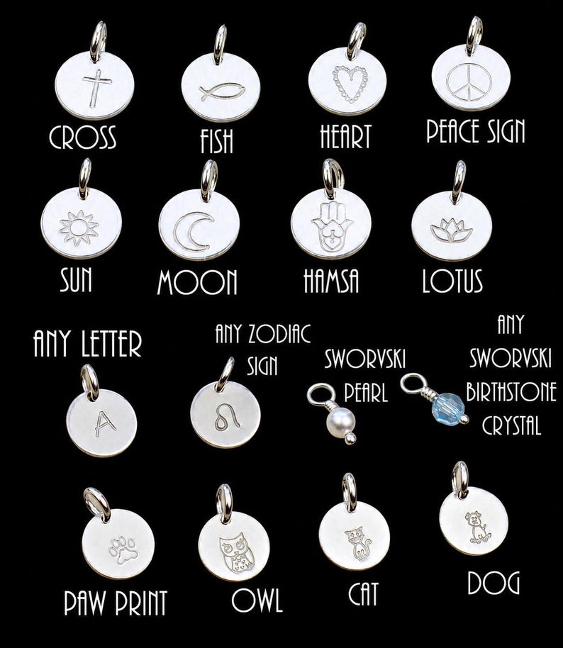 May include: A collection of silver-toned circular charms featuring engraved symbols including a cross, fish, heart, peace sign, sun, moon, hamsa, lotus, letter A, zodiac sign, paw print, owl, cat, dog, a pearl, and a light blue crystal birthstone.