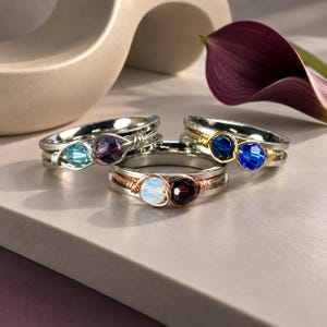 May include: Three wire-wrapped rings featuring faceted crystal beads. One silver-tone ring has light blue and purple beads, another silver-tone ring has two dark blue beads, and one has a rose gold-tone wire with an iridescent and a dark red bead.