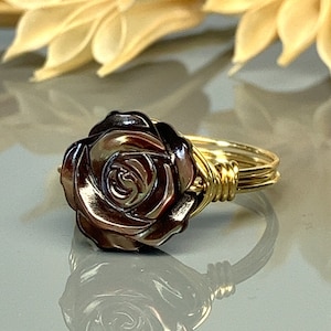 May include: A gold wire wrapped ring featuring a dark brown, rose-shaped, mother of pearl stone.