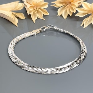 May include: A silver chain bracelet with a braided design. The bracelet is made of multiple strands of silver chain that are woven together to create a unique and stylish look.