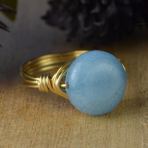 May include: A gold wire wrapped ring with a light blue round gemstone.
