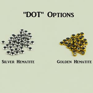 May include: Two piles of small, round, donut-shaped beads labeled "DOT" OPTIONS. The left pile consists of silver-colored hematite beads, and the right pile consists of golden-colored hematite beads. Each bead has a dark center hole.