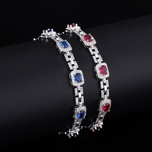 Può includere: Due braccialetti d'argento con pietre preziose blu e rosse alternate. Ogni braccialetto presenta pietre quadrate circondate da cristalli chiari più piccoli. I braccialetti sono esposti su uno sfondo scuro, evidenziando la loro lucentezza e il design.