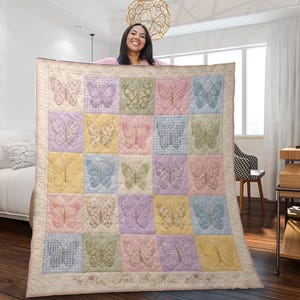 Può includere: Una trapunta dai colori pastello con un design patchwork con farfalle ricamate in vari colori e motivi. La trapunta ha un bordo color crema e il testo "For Sophia" è ricamato in basso. La trapunta è tenuta da una persona.