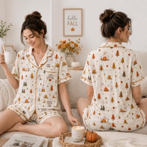 Peut inclure: Un ensemble de pyjama deux pièces composé d'une chemise à manches courtes boutonnée et d'un short assorti. Le tissu crème présente un motif répétitif de fantômes, de sapins, de feux de camp et de feuilles d'automne dans des tons orange et marron.