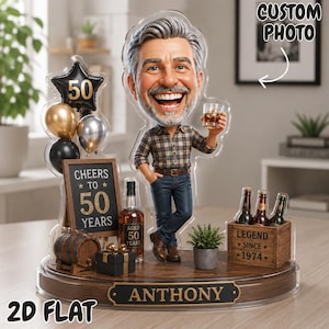 Könnte beinhalten: Ein flaches 2D-Acryl-Display mit einer Karikatur eines Mannes, der ein Glas Whiskey hält. Der Sockel enthält ein Holzschild mit der Aufschrift ANTHONY, ein Miniaturfass, ein Geschenk, ein Schild mit CHEERS TO 50 YEARS und eine Kiste mit LEGEND SINCE 1974.