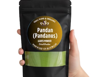 Pode incluir: Um saco preto de pó de folhas de Pandan segurado por uma mão. O saco tem uma janela transparente mostrando o pó verde. Um rótulo circular diz "100% Pure & Organic Pandan (Pandanus) Leaves Powder". O site também é visível.