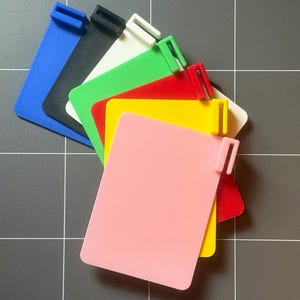 Może przedstawiać: Kolekcja kolorowych, prostokątnych plastikowych etykiet w różnych kolorach, w tym niebieskim, czarnym, białym, zielonym, czerwonym, żółtym i różowym. Każda etykieta ma mały, prostokątny klips na górze.