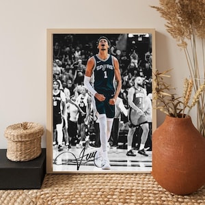 May include: Framed black and white photograph of a basketball player in a Spurs jersey, number 1. The player is celebrating with arms raised. The image is signed. The background shows a crowd of people.