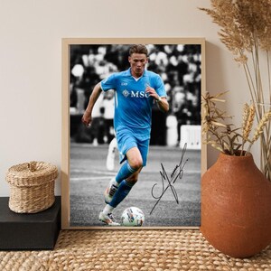 Könnte beinhalten: Gerahmter Druck mit einem Fußballspieler in hellblauem Trikot, der mit einem Fußball rennt. Der Hintergrund ist in Schwarzweiß gehalten. Die Unterschrift des Spielers ist sichtbar. Der Rahmen ist hellbraun.