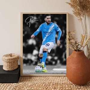 Puede incluir: Impresión enmarcada de un futbolista con una camiseta azul claro con el número 10, pateando un balón de fútbol. La firma del jugador está en la esquina superior izquierda. El fondo es en blanco y negro. El marco es marrón claro.