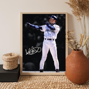 May include: Framed photograph of a baseball player in a white and blue uniform, with the word "MARINERS" on the front. The player is in a batting stance, with a signature in the lower left corner. The background is blurred.