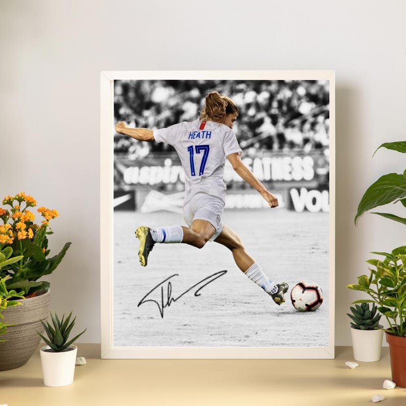 May include: Framed black and white photograph of a soccer player in a white uniform with the number 17 and the name "Heath" on the back, kicking a soccer ball. The photograph is signed and displayed in a white frame.
