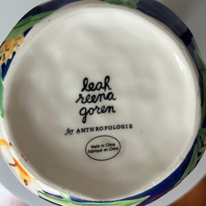 Puede incluir: La base de un jarr&oacute;n de cer&aacute;mica blanco con un dise&ntilde;o floral. El jarr&oacute;n est&aacute; marcado "leah reena goren for ANTHROPOLOGIE" y tiene una etiqueta que dice "Made in China Fabriqu&eacute; en Chine."