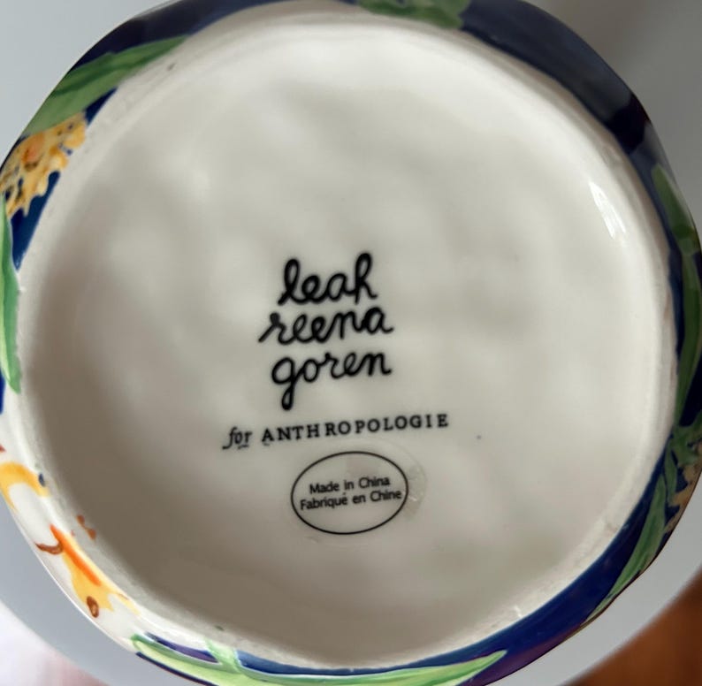 Puede incluir: La base de un jarr&oacute;n de cer&aacute;mica blanco con un dise&ntilde;o floral. El jarr&oacute;n est&aacute; marcado "leah reena goren for ANTHROPOLOGIE" y tiene una etiqueta que dice "Made in China Fabriqu&eacute; en Chine."