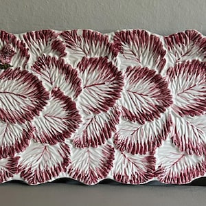 May include: A rectangular ceramic serving platter featuring a raised, embossed pattern of overlapping leaves in white and deep magenta. The edges of the platter are shaped like green, textured vine stems with small, textured berry-like accents.